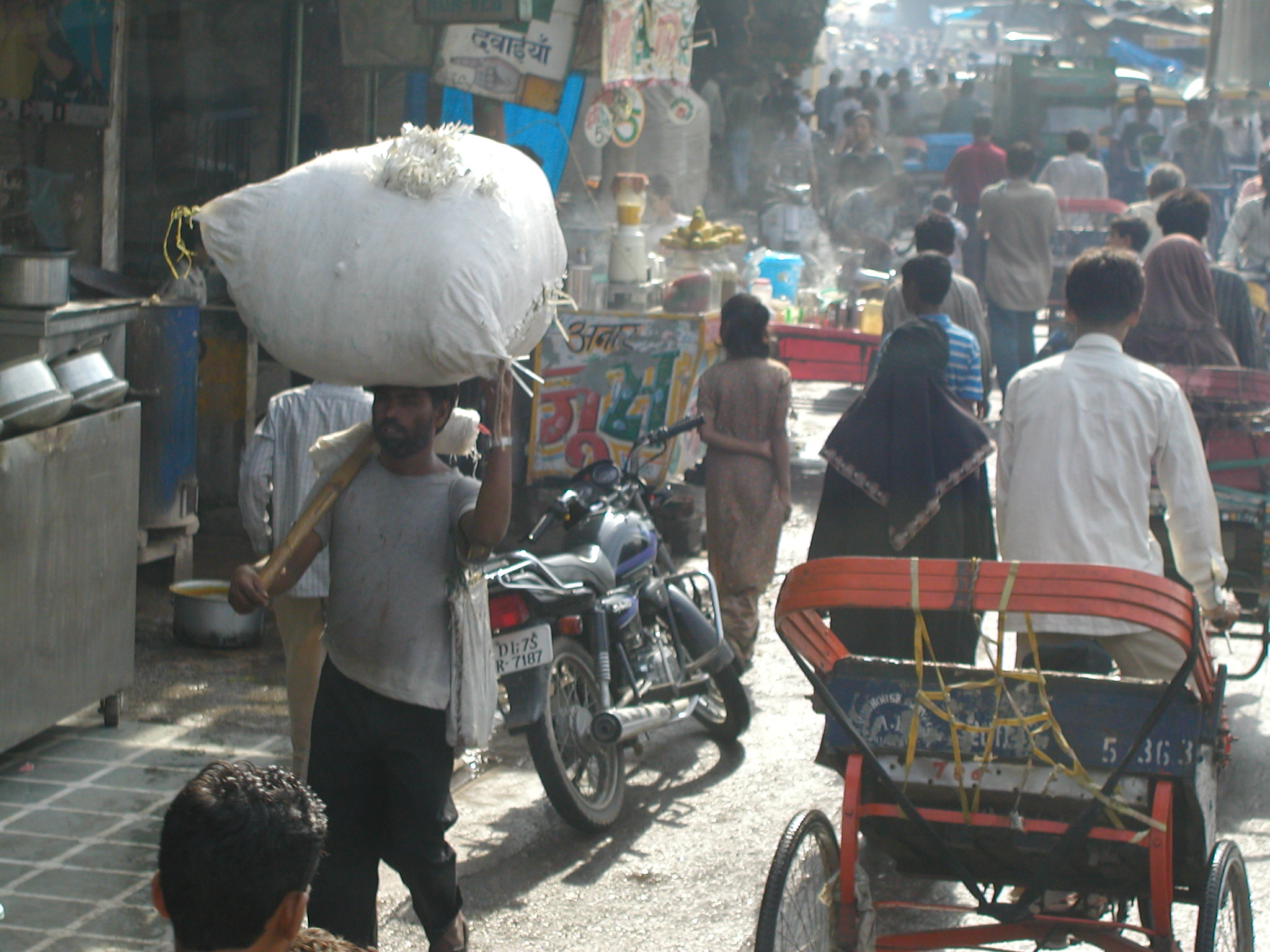 Carts, pedestrians, goods, and shops line the street of Delhi