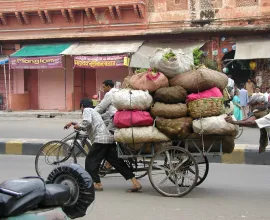 A man carries his load of goods on the back of his cart.