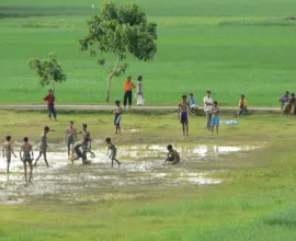 A group of children play a game on a field, possibly football (soccer).