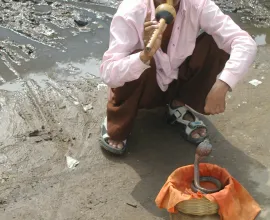 A snake charmer charms a snake as a form of street entertainment.